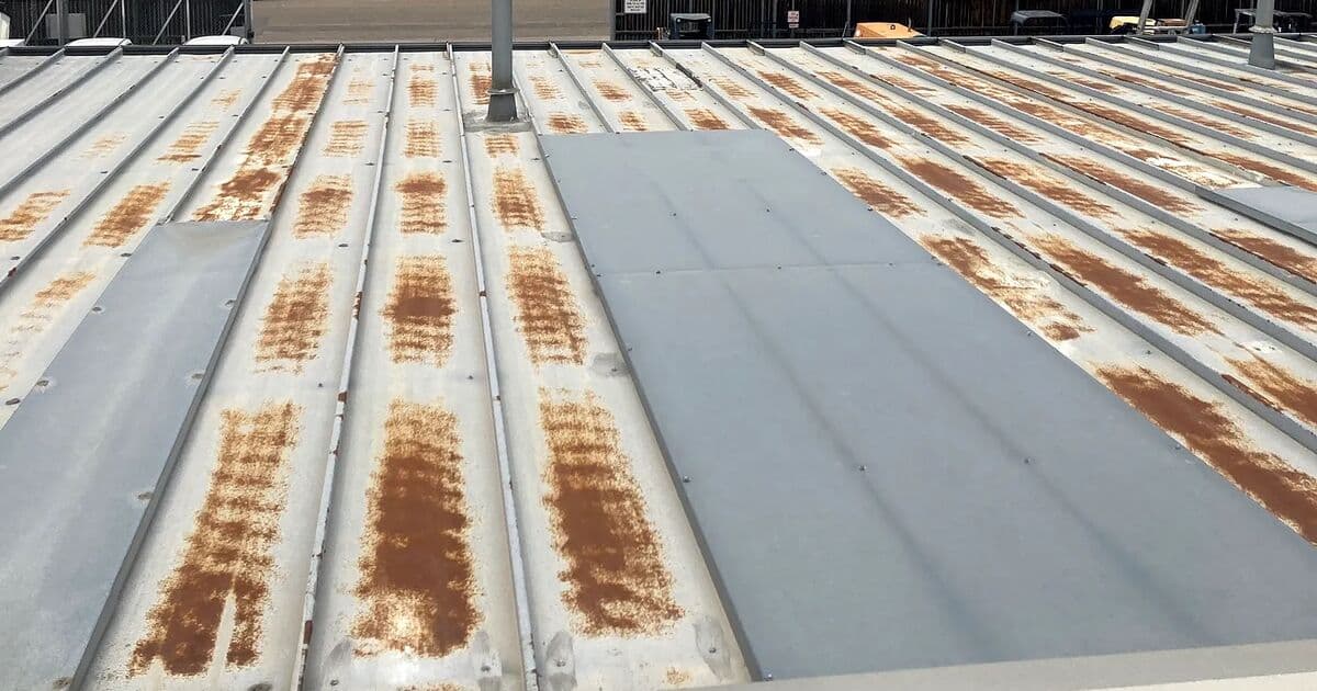 Rust streaks running along the ribs and fastener lines of an exposed-fastener metal roof on a commercial building in Denver, Colorado, before CRC restored it