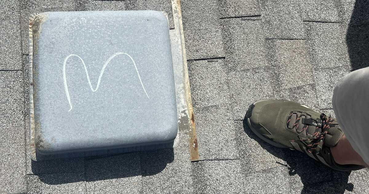 A galvanised roof vent cap on a Colorado commercial shingle roof, marked with chalk where hail struck the soft metal, with a roof inspector's boot beside it