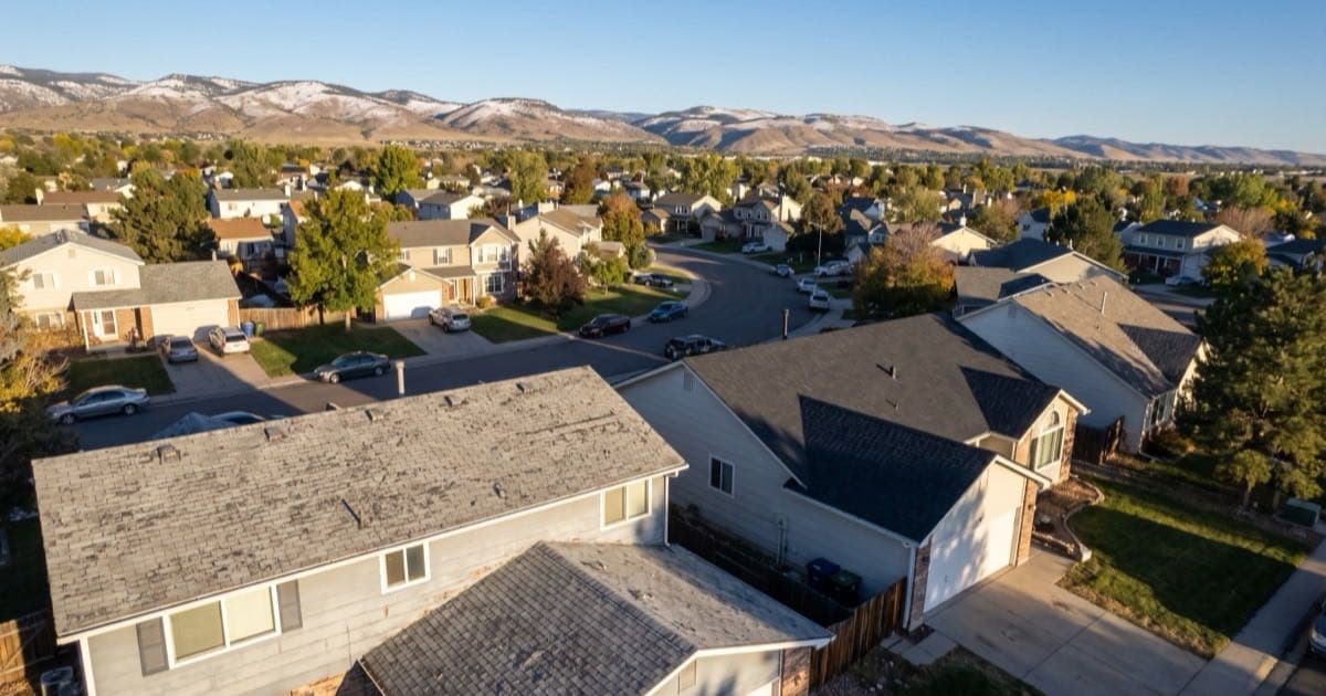 Illustrative representation of a Colorado Front Range neighborhood seen from above, showing roofs at different ages against snow-dusted foothills
